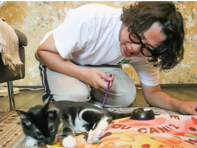 自宅のリビングで猫用のおもちゃで遊ぶ、梅崎さんと保護猫のキッス
